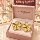 Cassandra gold-tone flower earrings in a pink Audrey Roman Jewels box on a boutique counter.