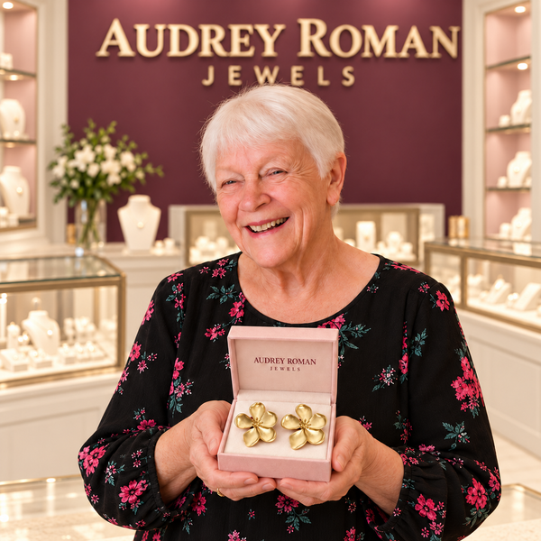 Woman presenting Cassandra flower earrings in an Audrey Roman Jewels box inside an ivory, rose and wine-colored boutique.