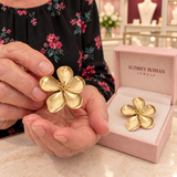 Cassandra gold-tone flower earring held above a pink presentation box inside the boutique.